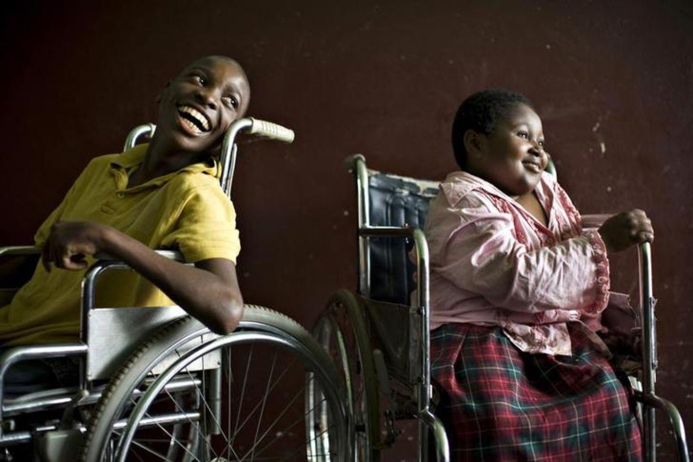 A boy and a girl both in wheelchairs looking on the right and smiling