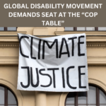 Heading that reads: Global disability movement demands seat at the “COP table”, underneath a picture shows a banner hanging that reads: Climate Justice