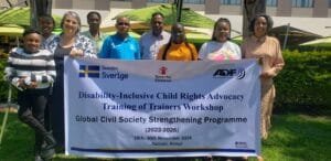Participant and trainers standing together holding a banner that reads: Disability Inclusive Child Rights Advocacy Training of Trainers Workshop