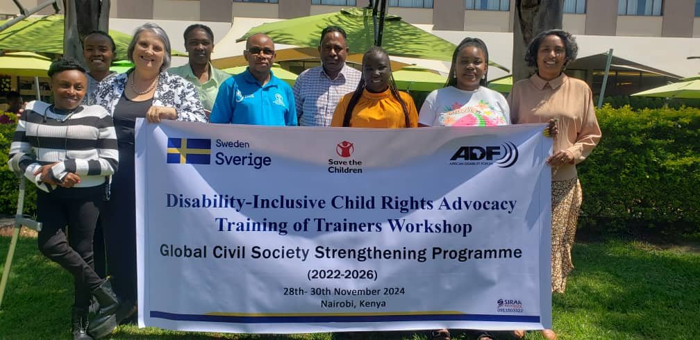Participant and trainers standing together holding a banner that reads: Disability Inclusive Child Rights Advocacy Training of Trainers Workshop