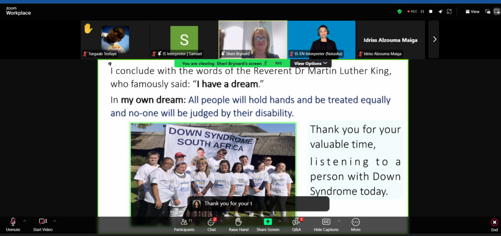 A Zoom webinar screenshot shows a slide presentation with an inspirational quote referencing Martin Luther King Jr.'s 'I have a dream' speech. The slide expresses a vision for equality, stating, 'All people will hold hands and be treated equally, and no one will be judged by their disability.' Below the text is a photo of a group of people with Down syndrome wearing matching white t-shirts and standing together in front of a banner that reads 'Down Syndrome South Africa.' The slide also thanks the audience for listening to a person with Down syndrome. The Zoom interface displays multiple participants, including interpreters, a speaker named Sheri Brynard, and a raised hand from a participant.