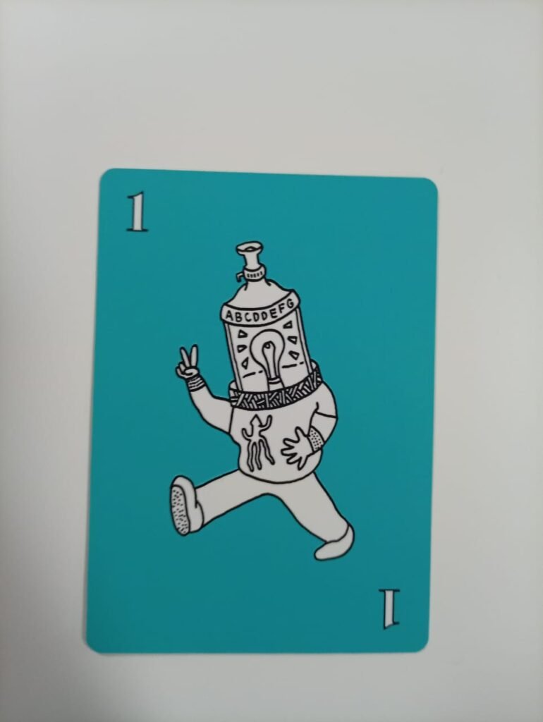 Card used during training depicts a stylized figure with a bottle-shaped head labeled with letters, walking forward while making a peace sign. The figure has a lightbulb illustrated on its body, set against a teal background, with the number “1” and the letter “I” shown on the card.