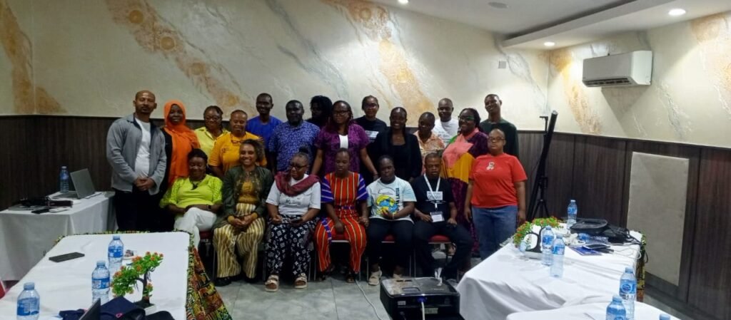 A diverse group of 20 people, some seated and others standing, pose in a warmly lit room with marble-textured walls during the mission in Abuja, Nigeria.