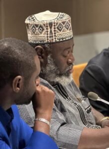Idriss, ADF Chairperson, speaks at the COSP19 while three colleagues listen with microphones and papers in front of them