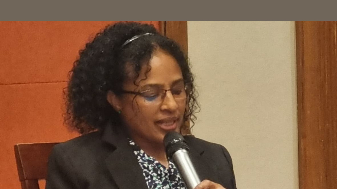 Shitaye Astawes, speaks into a microphone while reading from a laptop. She is seated in front of a wooden panel and cream wall. The image includes a heading at the top in bold white text on a brown background that reads: “ADF'S KEYNOTE ADDRESS ON ADVANCING ACCESS TO JUSTICE FOR PERSONS WITH DISABILITIES IN AFRICA.”||