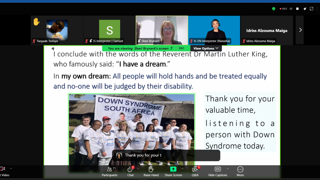 A Zoom webinar screenshot shows a slide presentation with an inspirational quote referencing Martin Luther King Jr.'s 'I have a dream' speech. The slide expresses a vision for equality, stating, 'All people will hold hands and be treated equally, and no one will be judged by their disability.' Below the text is a photo of a group of people with Down syndrome wearing matching white t-shirts and standing together in front of a banner that reads 'Down Syndrome South Africa.' The slide also thanks the audience for listening to a person with Down syndrome. The Zoom interface displays multiple participants, including interpreters, a speaker named Sheri Brynard, and a raised hand from a participant.