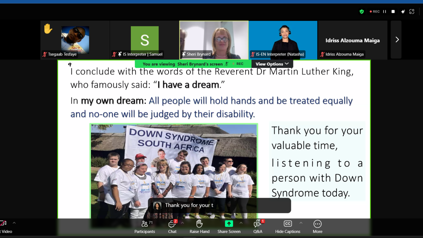 A Zoom webinar screenshot shows a slide presentation with an inspirational quote referencing Martin Luther King Jr.'s 'I have a dream' speech. The slide expresses a vision for equality, stating, 'All people will hold hands and be treated equally, and no one will be judged by their disability.' Below the text is a photo of a group of people with Down syndrome wearing matching white t-shirts and standing together in front of a banner that reads 'Down Syndrome South Africa.' The slide also thanks the audience for listening to a person with Down syndrome. The Zoom interface displays multiple participants, including interpreters, a speaker named Sheri Brynard, and a raised hand from a participant.