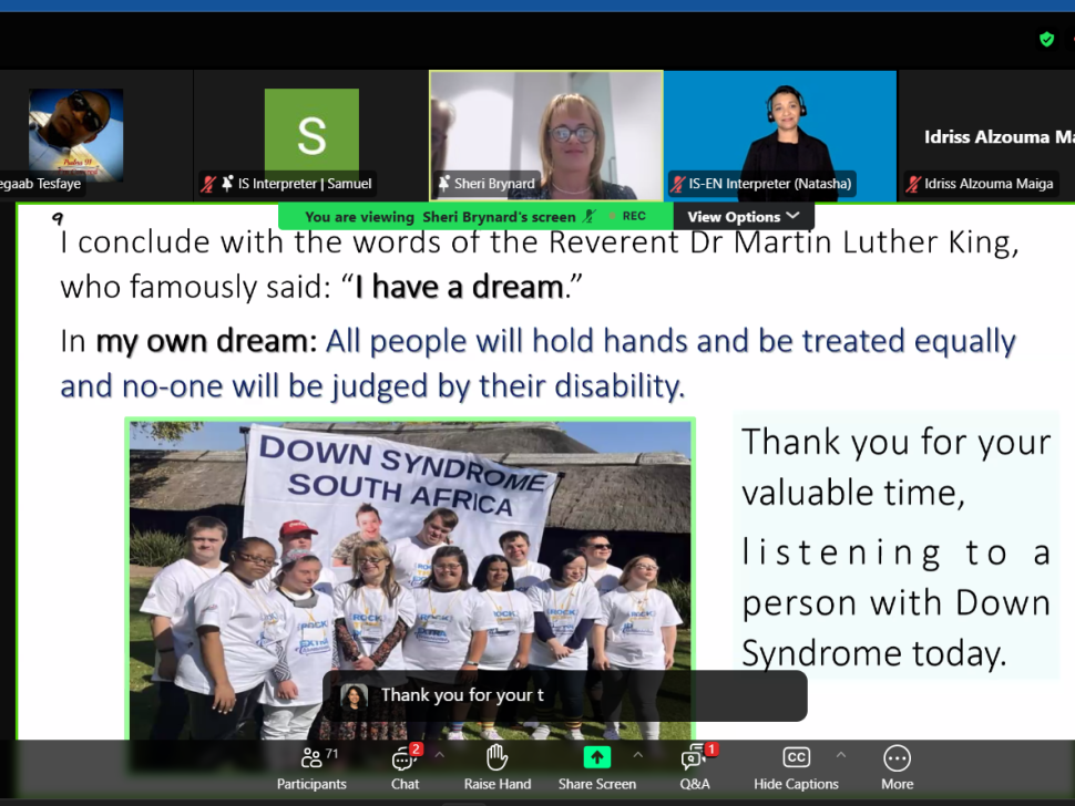 A Zoom webinar screenshot shows a slide presentation with an inspirational quote referencing Martin Luther King Jr.'s 'I have a dream' speech. The slide expresses a vision for equality, stating, 'All people will hold hands and be treated equally, and no one will be judged by their disability.' Below the text is a photo of a group of people with Down syndrome wearing matching white t-shirts and standing together in front of a banner that reads 'Down Syndrome South Africa.' The slide also thanks the audience for listening to a person with Down syndrome. The Zoom interface displays multiple participants, including interpreters, a speaker named Sheri Brynard, and a raised hand from a participant.