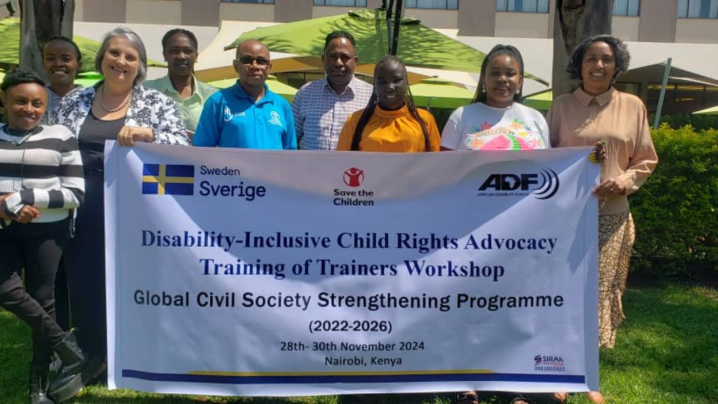 Participant and trainers standing together holding a banner that reads: Disability Inclusive Child Rights Advocacy Training of Trainers Workshop