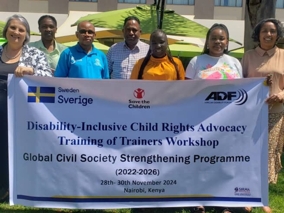 Participant and trainers standing together holding a banner that reads: Disability Inclusive Child Rights Advocacy Training of Trainers Workshop