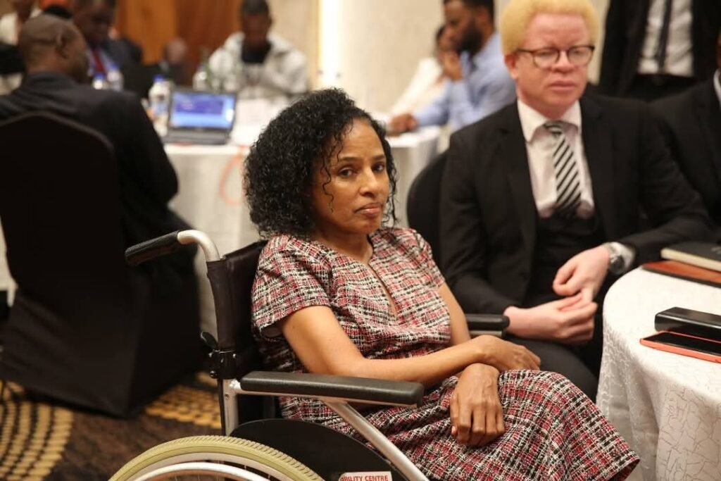 Image of Shitaye Astawes, sitting at a table in a wheelchair.