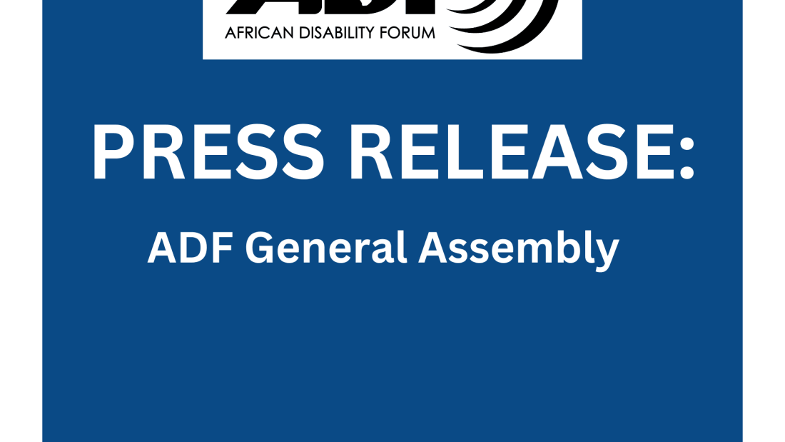 |A large group of people sit in a conference room, attentively listening and taking notes. Some have laptops open. Posters and presentation slides are visible on the walls.|ADF Chair Idriss Maiga in a wheelchair participates in a conference session, surrounded by other attendees seated at tables covered with documents and laptops. Everyone appears engaged in the discussion.
